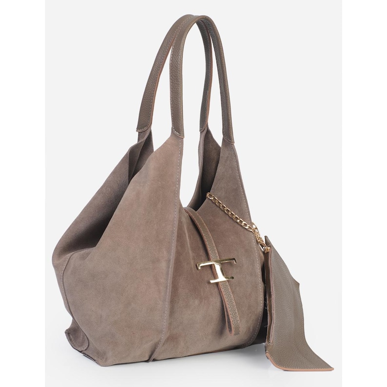 May include: A taupe suede shoulder bag with long handles. The bag features a gold-tone chain and a gold-tone metal accent. A matching pouch is attached to the side. The bag has a soft, slouchy design.