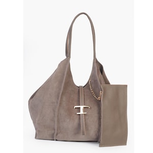 May include: A taupe suede tote bag with a matching pouch. The bag features a long handle, a gold-tone metal accent, and a delicate chain detail. The pouch is a rectangular shape and is made of a smooth leather material.