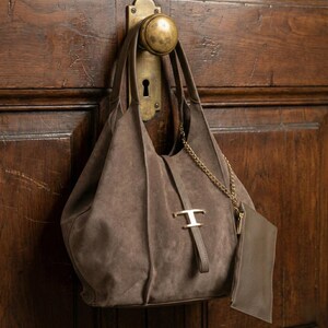 May include: A brown suede shoulder bag with a gold-tone chain and hardware, hanging from a brass doorknob. The bag has a matching small pouch attached. The bag is a soft, slouchy style.