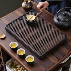 以下が含まれることがあります： 黒いティーポット、小さな黒いティーカップ、黒と金のティーサーバーを備えた、スラットデザインの木製ティートレイ。 ティーセットは濃い色の木製のテーブルに配置されており、穏やかなお茶の儀式のセッティングを作り出しています。