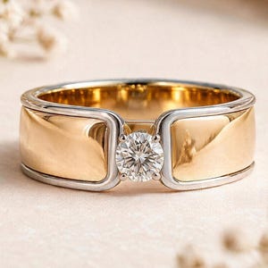 Peut inclure: Une bague bicolore composée d'un large anneau en or jaune poli avec des bords argentés et un diamant blanc unique taille brillant serti au centre. L'anneau métallique présente une surface lisse et réfléchissante au design structuré.