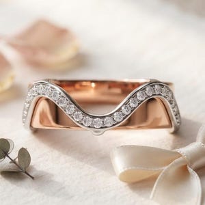 Peut inclure: Une bague incurvée dotée d'une surface intérieure en or rose et d'une couche extérieure argentée incrustée d'une rangée de petites pierres claires taillées en rond. La bague présente une silhouette ondulée suivant le contour des pierres.