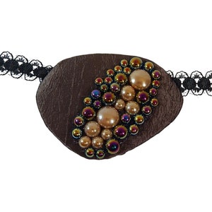 May include: A brown leather eye patch with a decorative design of iridescent and pearl-colored beads.