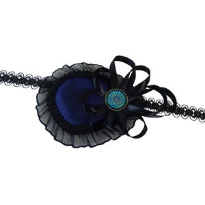 Op de afbeelding: Een blauw fluwelen ooglapje met zwarte kant en een zwarte satijnen strik met een blauw-groene knoop.