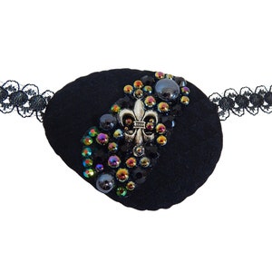 May include: Black eye patch with a silver fleur-de-lis and iridescent rhinestones.