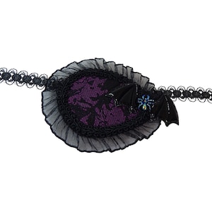 May include: A black eye patch with a purple lace trim and a black bat with a blue and green spider embellishment.