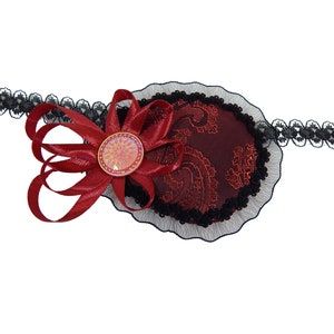 Pode incluir: Um tapa-olho vermelho com uma borda de renda preta e um laço vermelho com um botão rosa brilhante. O tapa-olho é preso a uma faixa elástica preta.
