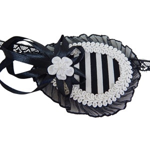 May include: Black and white striped eye patch with a white lace trim and a white flower accent. The eye patch is attached to a black lace headband.