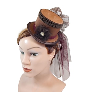 May include: A brown top hat with a black band and a small burgundy veil. The hat is decorated with a black flower with a pearl center.