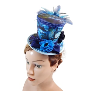 May include: Miniature top hat in shades of blue, featuring a floral design and feathers. The hat has a small brim and is adorned with a blue bow and flower. A decorative accessory for themed events.
