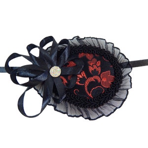 Puede incluir: Un parche para el ojo negro con un diseño floral rojo y negro, un lazo de satén negro con un strass y un borde de encaje negro.
