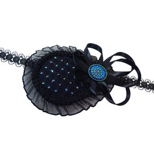 Può includere: Parche per l'occhio nero con bordino in pizzo nero e un bottone gioiello blu e verde. Il parocchietto è attaccato a un cerchietto in pizzo nero.