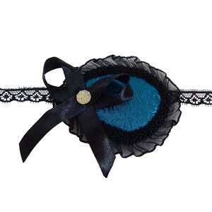 Pode incluir: Um tapa-olho azul com acabamento em renda preta e um laço de cetim preto. O tapa-olho é decorado com um pequeno strass.