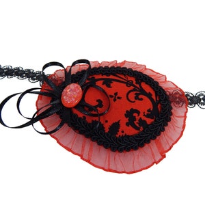 Pode incluir: Um tapa-olho vermelho e preto com um design floral e uma faixa de renda preta. O tapa-olho tem um tecido vermelho com um padrão floral preto e uma borda preta. A faixa é feita de renda preta.