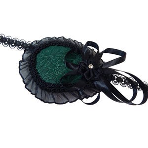 May include: A black eye patch with a green velvet center and a black lace trim. The eye patch is attached to a black ribbon and lace headband.