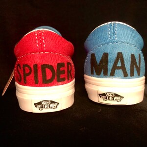 May include: A pair of red and blue Vans slip-on shoes with the words "Spider" and "Man" written on the back of each shoe.