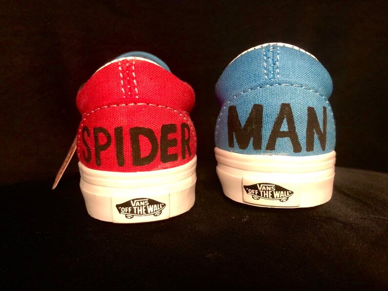 May include: A pair of red and blue Vans slip-on shoes with the words "Spider" and "Man" written on the back of each shoe.