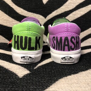 Może przedstawiać: Para zielono-fioletowych but&oacute;w Vans slip-on z napisami "Hulk" i "Smash" w kolorze czarnym.