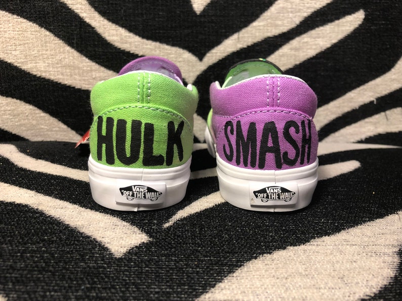 Może przedstawiać: Para zielono-fioletowych but&oacute;w Vans slip-on z napisami "Hulk" i "Smash" w kolorze czarnym.