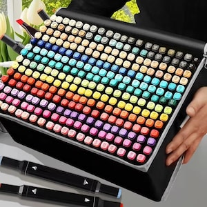 May include: A black carrying case filled with a rainbow assortment of art markers. The markers are arranged in a grid, showcasing a wide spectrum of colors. Two black markers with colored tips are in the foreground, suggesting a complete art set.