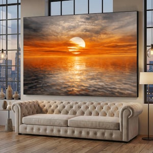 Könnte beinhalten: Große, gerahmte Leinwandkunst, die einen Sonnenuntergang über dem Wasser darstellt. Der Himmel geht von Grau in Orange über, wobei sich die Sonne auf der Wasseroberfläche spiegelt. Das Kunstwerk hängt über einem beigefarbenen, getufteten Sofa.