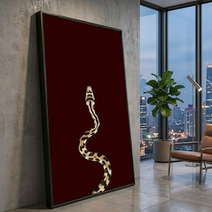 May include: Framed art print featuring a detailed illustration of a snake against a deep red background. The snake has a pattern of black and tan spots and stripes. The artwork is displayed in a black frame.