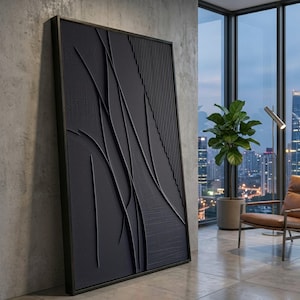 Könnte beinhalten: Große, schwarze abstrakte Wandkunst mit strukturierter Oberfläche und dunklem Rahmen. Das Kunstwerk zeigt fließende, geschwungene Linien und vertikale Rippen, die ein modernes, minimalistisches Design schaffen. Das Stück lehnt an einer Betonwand in einem gut beleuchteten Raum.