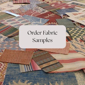 May include: A selection of fabric swatches in diverse patterns and colours, including floral, striped, and geometric designs. The swatches are arranged on a surface, with a sign that reads "Order Fabric Samples". The fabrics feature shades of blue, red, and beige.