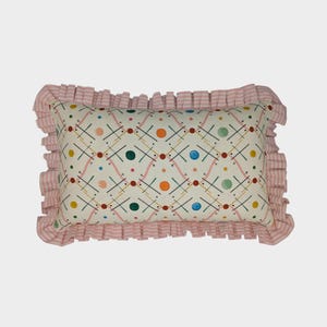 May include: Rectangular cushion with a cream background and a colourful geometric pattern of lines and dots. The cushion has a pink and white striped frill trim.