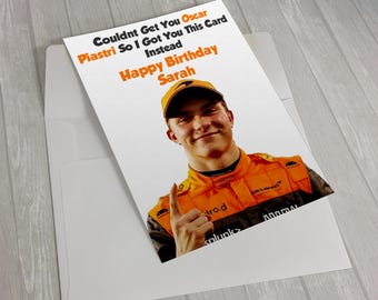 May include: A white greeting card with a photo of a smiling man in a racing uniform. The card reads "Couldnt Get You Oscar Piastri So I Got You This Card Instead Happy Birthday Sarah."