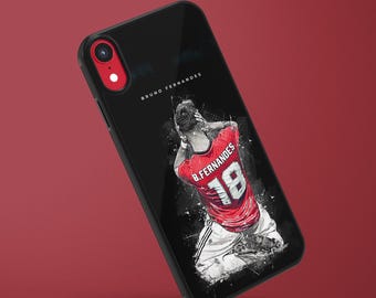 May include: Black phone case featuring a stylized image of a soccer player in a red jersey with the number 18. The player's name, B. Fernandes, is visible on the jersey. The phone case has a red camera lens ring and the name "BRUNO FERNANDES" is printed on the case.