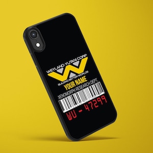 Peut inclure: Coque de téléphone noire avec le logo Weyland-Yutani Corp en jaune et blanc. Le texte "BUILDING BETTER WORLDS", "YOUR NAME", "XENOMORPH RESEARCH DEPT." et un code-barres sont présents. Le numéro "WU - 47299" est affiché en rouge.