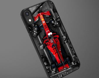 May include: A black smartphone case featuring a top-down view of a bright red Formula 1 race car in a pit stop. The car displays the number 16 and various sponsor logos. Pit crew members in black uniforms are positioned around the vehicle on a track.