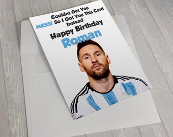 May include: A white birthday greeting card featuring a photograph of Lionel Messi wearing a light blue and white jersey. The text reads: "Couldnt Get You MESSI So I Got You This Card Instead Happy Birthday Roman" with the name Roman in blue.