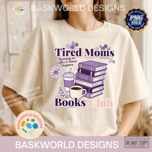 Op de afbeelding: Een crèmekleurig T-shirt met een afbeelding van een stapel paarse boeken, een koffiekopje en een beker. De tekst luidt "Tired Moms", "Running on coffee & chaos chapters" en "Books Club", versierd met kleine paarse en witte bloemillustraties.