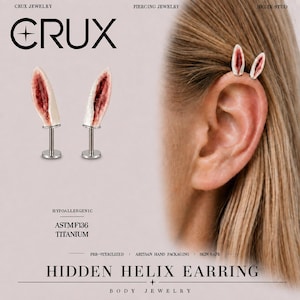 May include: A pair of helix stud earrings featuring a realistic, flesh-toned ear-shaped design with a deep red center. The studs are made of ASTM F136 titanium with a flat back post. The text CRUX JEWELRY and HIDDEN HELIX EARRING is visible.