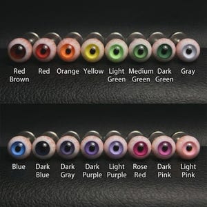 Könnte beinhalten: Eine Sammlung von augenförmigen Schmuckstücken in verschiedenen Farben, darunter rotbraun, orange, gelb, grün, blau, lila und rosa. Jedes Stück hat eine detaillierte Iris und Pupille, mit den Farbbezeichnungen darunter.