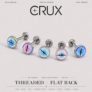 May include: Five silver-toned flat back labret studs featuring circular cabochon tops with realistic dragon eye designs in blue, green, and pink hues. The text CRUX, THREADED, FLAT BACK, and various piercing locations are printed on the image.