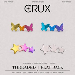 Puede incluir: Cuatro piezas de joyería corporal de metal con la marca CRUX. Dos presentan tres mariposas conectadas en degradado amarillo-naranja-rosa y azul-morado. Dos presentan tres estrellas conectadas en amarillo-rosa-morado y plata. Incluye THREADED FLAT BACK.