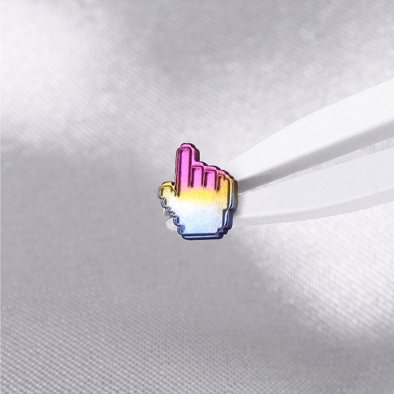 May include: A small metal pin shaped like a computer mouse cursor hand icon. The pin features a gradient finish that transitions from a vibrant pink at the top, through a bright yellow in the middle, to a deep blue at the bottom edge.