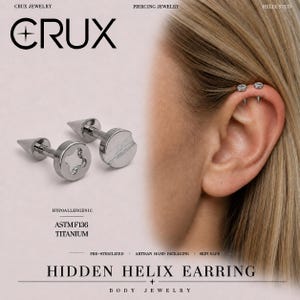 May include: A silver-colored titanium helix stud earring featuring a flat, circular head with a slotted screw design and a pointed spike back. The jewelry is labeled as hypoallergenic, ASTM F136 titanium, and pre-sterilized. Text includes CRUX JEWELRY.