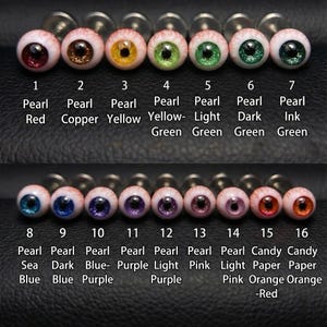 Puede incluir: Dieciséis cabujones redondos con forma de ojo dispuestos en dos filas, cada uno con una pupila negra central y un iris de color. Los colores incluyen rojo, cobre, amarillo, varios tonos de verde, azul, morado, rosa y naranja, numerados del 1 al 16.