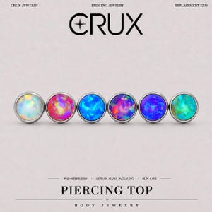 Puede incluir: Seis piezas superiores para piercing circulares con engastes de plata metálica y cabujones de estilo ópalo de colores. El texto dice CRUX JEWELRY, PIERCING JEWELRY, REPLACEMENT END, PRE-STERILIZED, ARTISAN HAND PACKAGING, SKIN SAFE, PIERCING TOP y BODY JEWELRY.