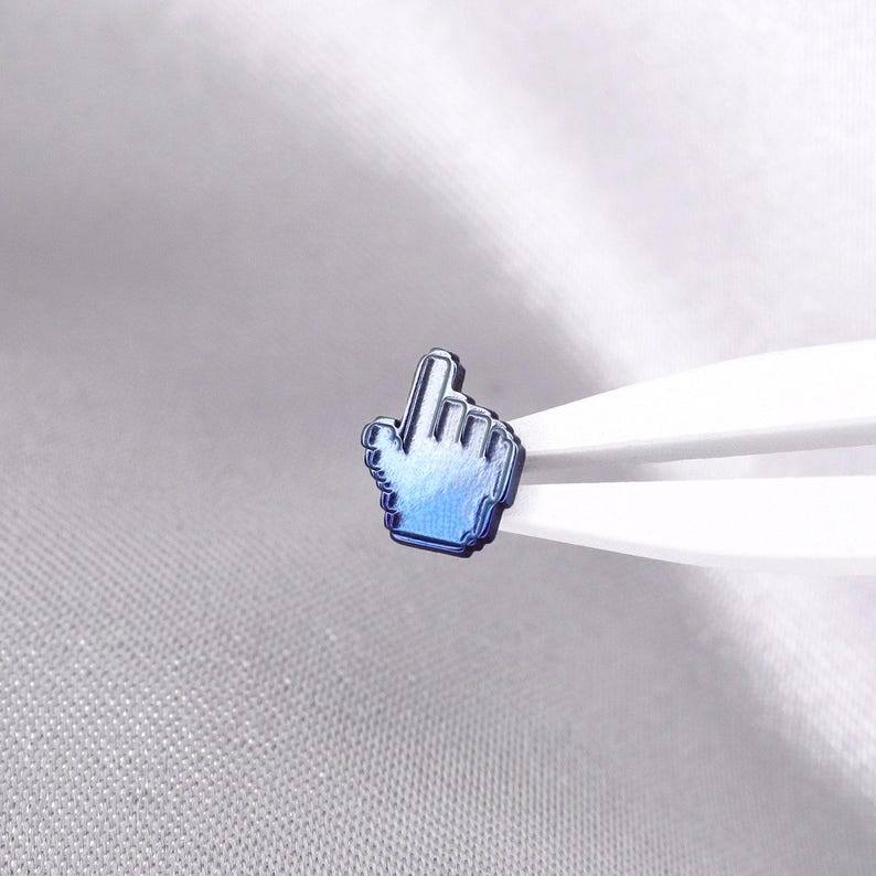 May include: A small, metallic blue pin shaped like a computer mouse cursor hand icon. The pin features a gradient finish transitioning from a deep navy blue at the base to a lighter, vibrant blue at the top, with a distinct pixelated edge design.