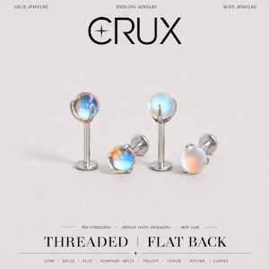 May include: Four silver-toned metal labret piercing studs with iridescent, spherical cabochon stones. Each piece features a flat back and a threaded post. The text CRUX, THREADED, FLAT BACK, and other labels are visible in the image.