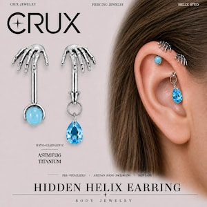 Può includere: Un orecchino helix color argento con un design a mano scheletrica sulla parte superiore. Una versione include una pietra rotonda azzurra, l'altra un cristallo azzurro a goccia pendente. Il testo include CRUX e HIDDEN HELIX EARRING.