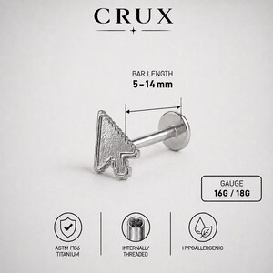 May include: A silver-colored titanium labret stud featuring a computer mouse cursor arrow design. The jewelry has a bar length of 5-14 mm and a gauge of 16G or 18G. It is internally threaded, hypoallergenic, and labeled with the brand name CRUX.