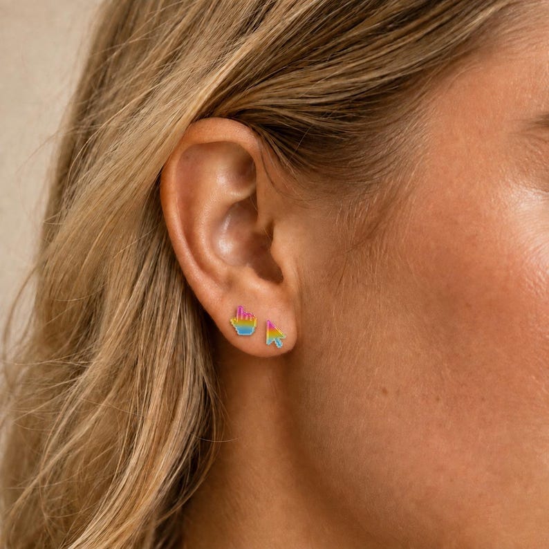 May include: A pair of small stud earrings featuring a computer mouse cursor and a pointing hand icon. Each earring has a gradient color scheme transitioning from pink to yellow to blue, designed as a set of two distinct shapes for the earlobe.