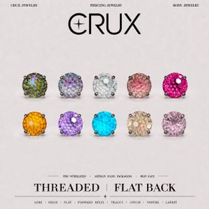 Può includere: Dieci borchie rotonde con pietre preziose sfaccettate per piercing, disposte su due file. Le borchie presentano vari colori tra cui verde, blu, bianco, rosa, magenta, arancione, viola, ciano, champagne e rosa chiaro, montate su supporti in metallo scuro.