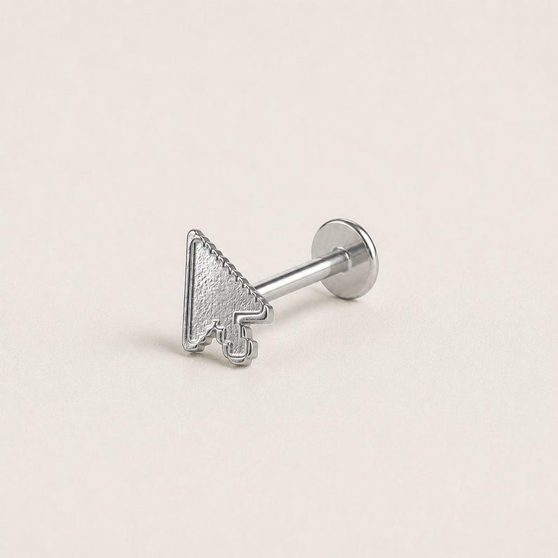 May include: A silver-toned labret stud body jewelry piece featuring a flat, textured computer mouse cursor arrow design at the front. The piece includes a straight post and a circular flat back disc, crafted from a metallic material with a matte finish.